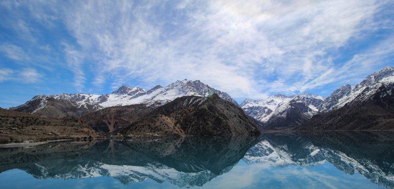 View of Iskander Kul lake with snow topped mountains behind in Tajikistan Fann mountains