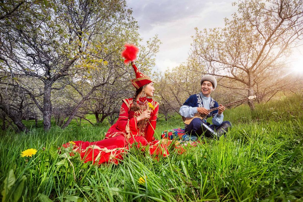 Kazakh man playing dombra and singing the song for woman in red on the green grass in Almaty, Kazakhstan, Central Asia