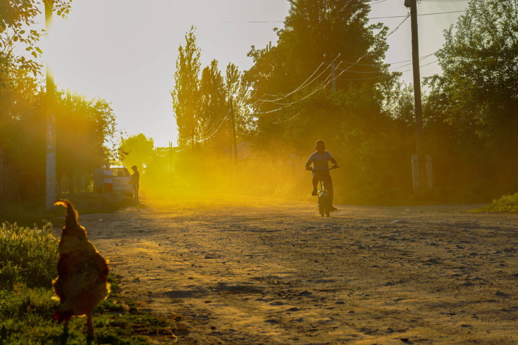 A boy riding with bike on a dirt road in Toktogul with a chicken in the foreground