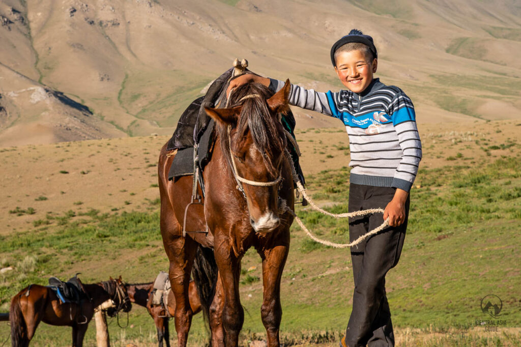 A young Kyrgyz boy smiling next to his horse.