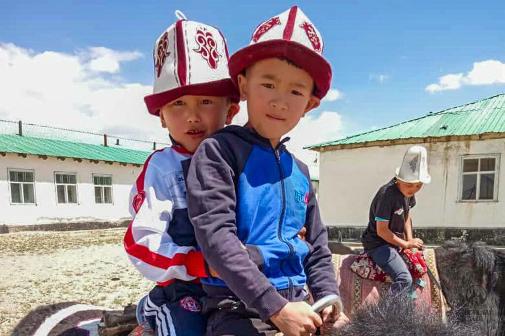 Bambini kirghisi che indossano kalpak nel Pamir a cavallo di yak