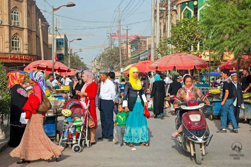 Gente uigur caminando por una calle comercial con ropa típica de la cultura uigur