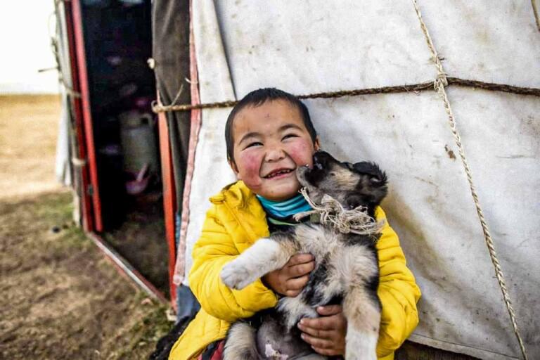 Kyrgyz child carrying a puppy next to a yurt at Son Kul lake