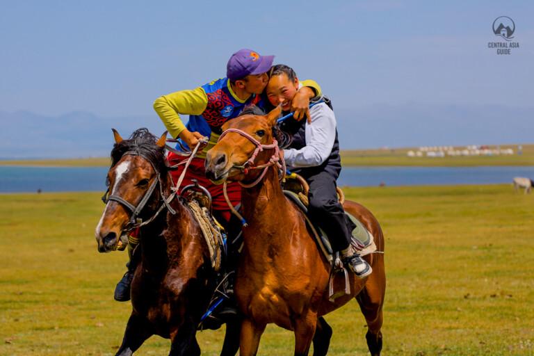 Kyrgyz man kissing a Kyrgyz girl after he managed to catch her riding with horse in Son Kul lake with yurts in the background